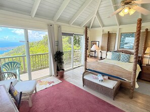 A bedroom with a four-poster bed, a balcony with a view, and a seating area with a chair and a table. - Discover Orchid Knoll – a Caribbean island retreat offering breathtaking views, a refreshing pool, and complete privacy! Don’t miss out on this incredible opportunity to unwind in a tropical setting. (Bordeaux Mountain)