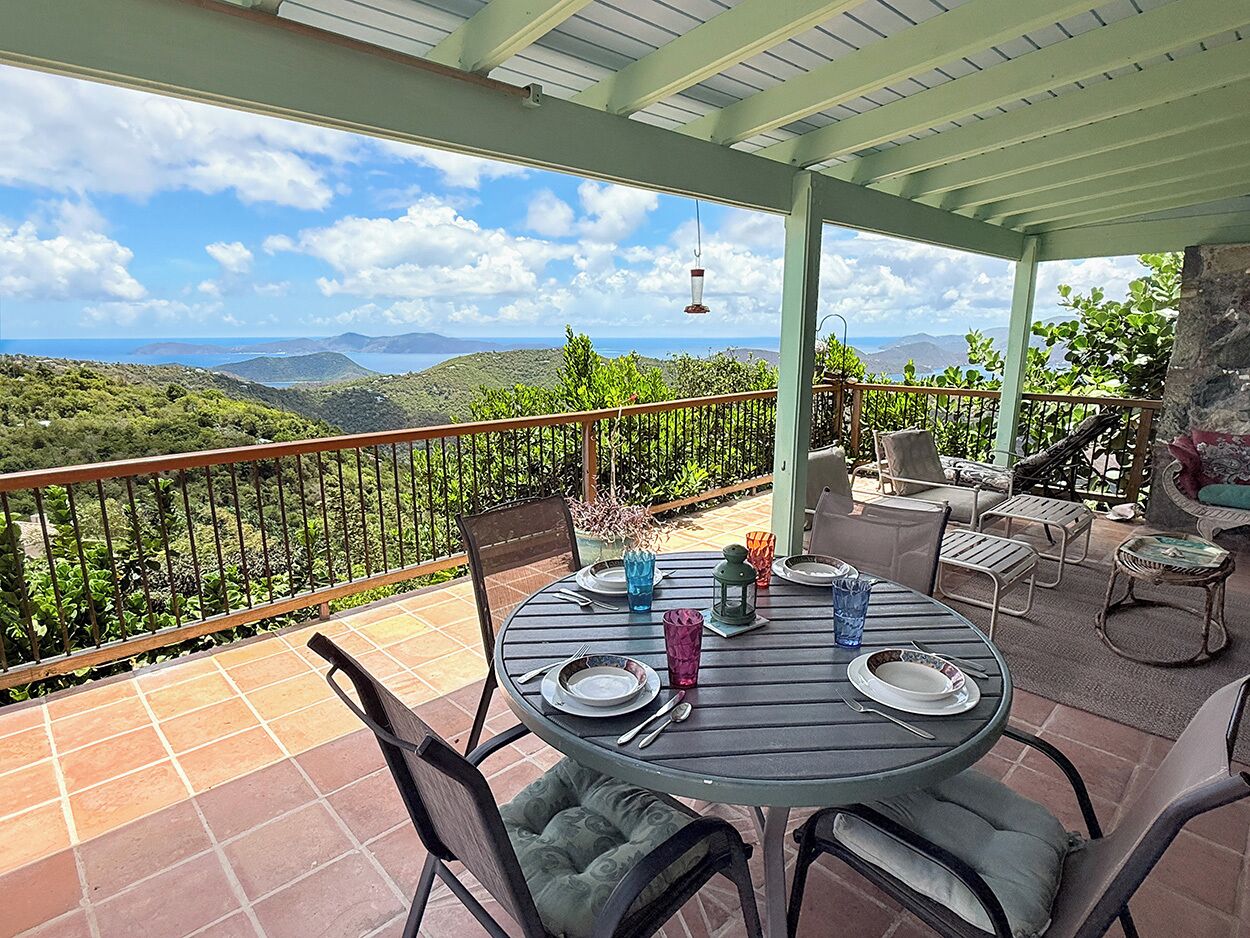 An outdoor patio with a table set for dining, surrounded by chairs, and overlooking a scenic landscape.