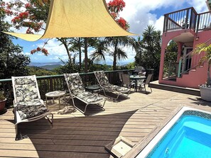 A wooden deck with lounge chairs and a pool, surrounded by tropical plants and a view of the landscape. - Discover Orchid Knoll – a Caribbean island retreat offering breathtaking views, a refreshing pool, and complete privacy! Don’t miss out on this incredible opportunity to unwind in a tropical setting. (Bordeaux Mountain)