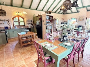 Un coin repas avec une table en bois dressée pour quatre personnes, entourée de chaises, et un espace cuisine comprenant un réfrigérateur et divers ustensiles.