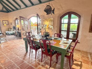 Un coin repas avec une table dressée pour quatre personnes, entourée de chaises rouges, dans une pièce dotée d’un sol carrelé et de fenêtres en arc de cercle.