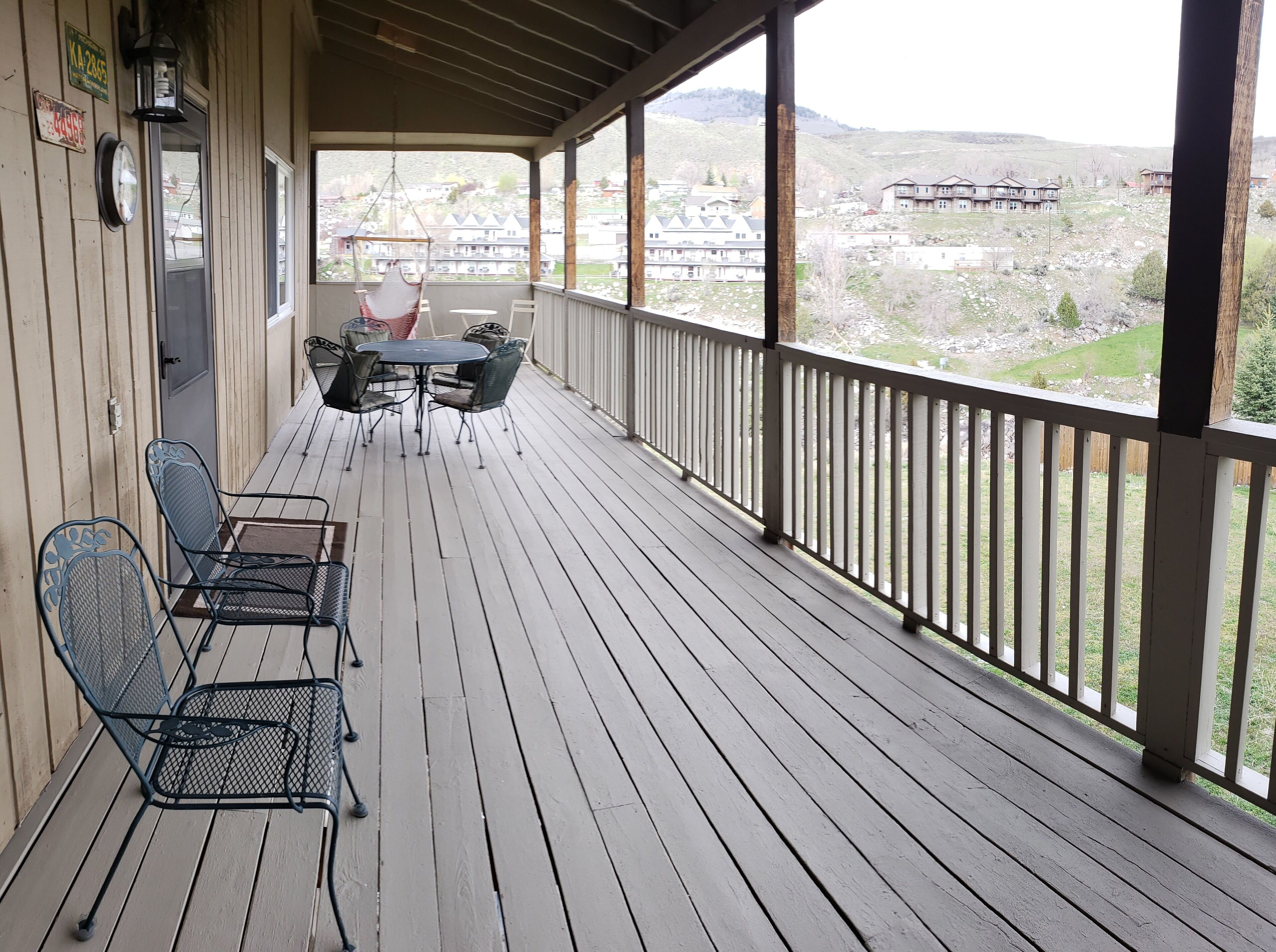 A wooden deck with outdoor seating, a hanging chair, and a view of a residential area.