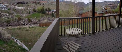 A wooden deck with a table and chairs, overlooking a residential area with houses and a river.