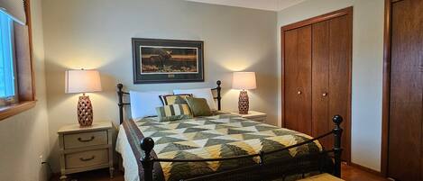 A bedroom with a bed, bedside lamps, a ceiling fan, a wooden bench, a framed picture on the wall, and a wardrobe.