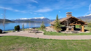 A lodge with a stone chimney, wooden deck, picnic tables, and a view of a lake and mountains. - Keystone 4BR Townhome at River Run Base - Prices lowered for open dates! (Keystone)