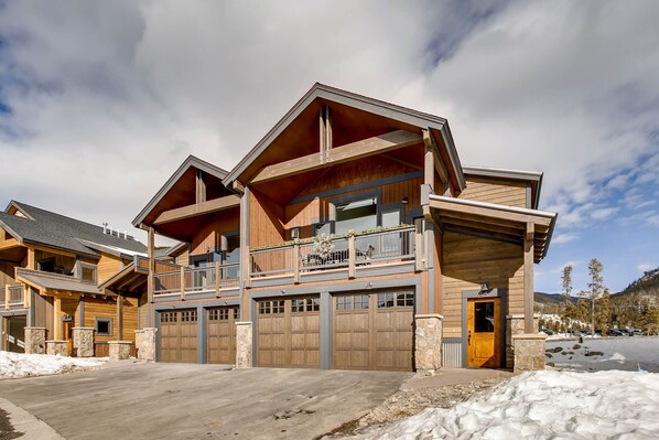 A large, multi-story wooden building with a prominent balcony, multiple garage doors, and a snow-covered landscape.