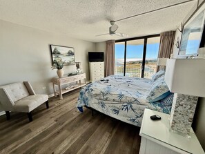 A bedroom with a bed, a desk, a chair, a TV, and a balcony with a view.