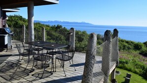 An outdoor patio with a table and chairs, overlooking a scenic view of the ocean and mountains. - Experience Alaska! Amazing Views! Check out a walk through video tour (Homer)
