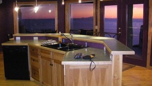 A kitchen with wooden cabinets, a sink, and a dishwasher. There are pendant lights above the counter. - Experience Alaska! Amazing Views! Check out a walk through video tour (Homer)