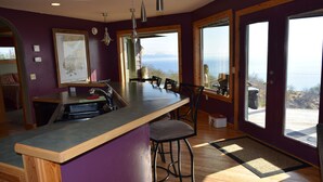 A kitchen with a large island, bar stools, and a view of the outdoors. - Experience Alaska! Amazing Views! Check out a walk through video tour (Homer)