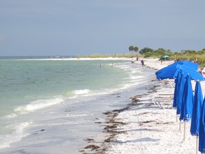 Ein Strand mit klarem Wasser, weißem Sand und blauen Sonnenschirmen.