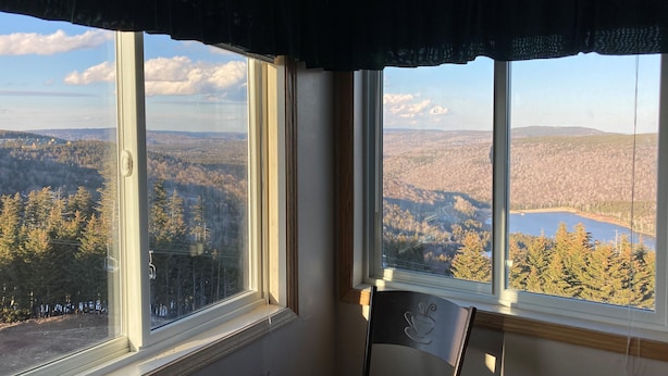 A room with a large window offering a view of a forested landscape and a lake. - Ski-in/Ski-out, Penthouse Unit w/ Awesome Views, Walk to Village! (Snowshoe)