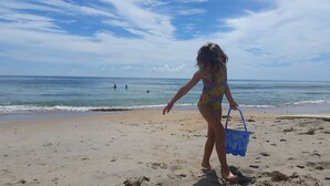 Una playa con una persona traje de baño colorido caminando hacia el agua, sosteniendo un bolso azul.