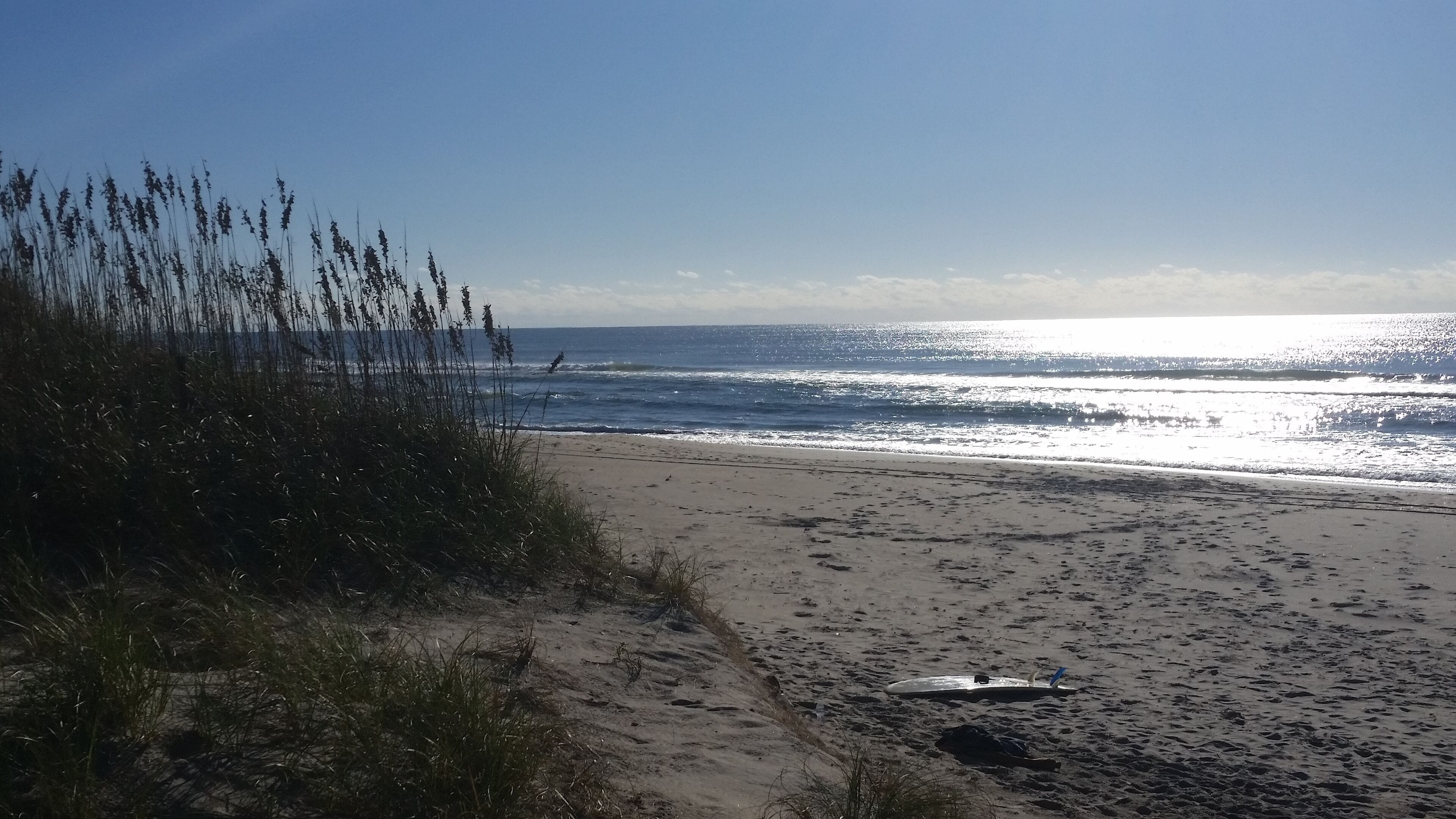 A sandy beach with waves, a surfboard, and tall grasses.