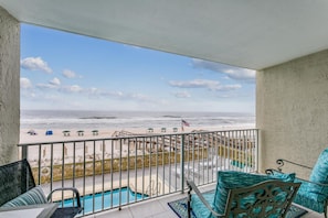 Un balcón con vista a la playa, una piscina y mobiliario exterior.