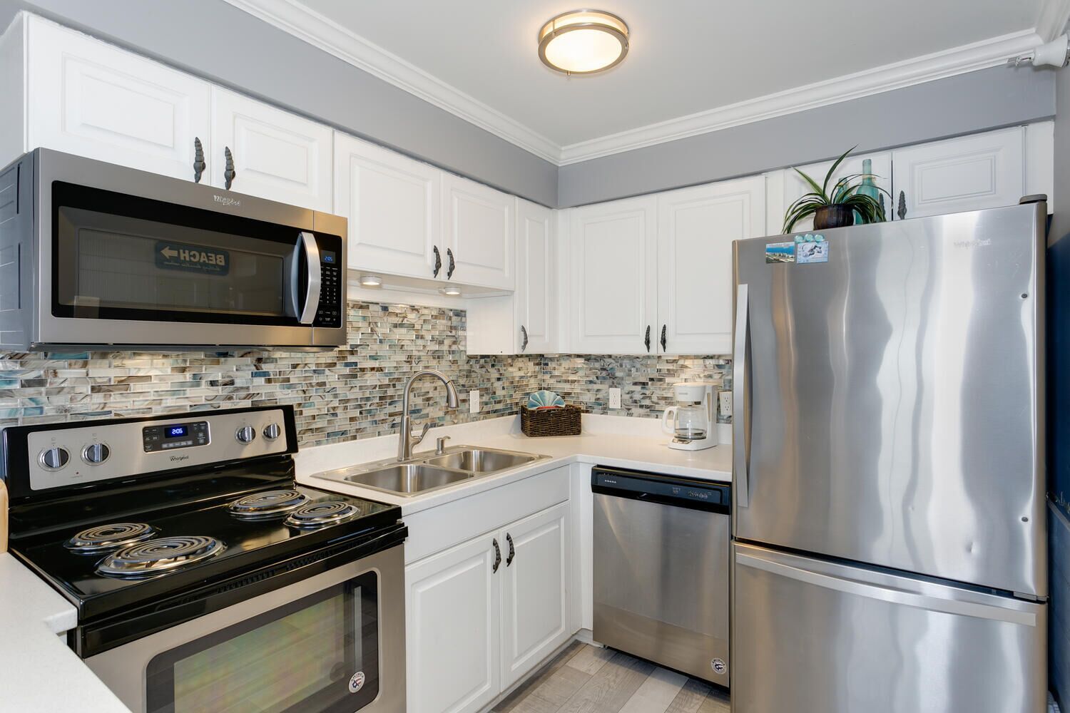 A modern kitchen with white cabinets, a stainless steel refrigerator, a built-in microwave, a stove, and a dishwasher.