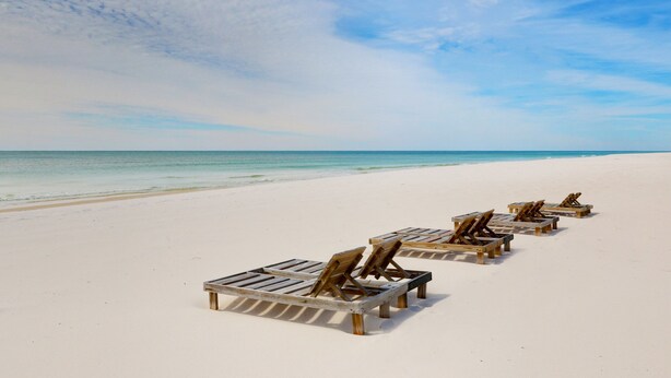 A beach with wooden lounge chairs aligned in a row. - BEST DEAL ON THE KEY! Updated Gulf Front Condo! Full Ocean Views! (Pensacola)