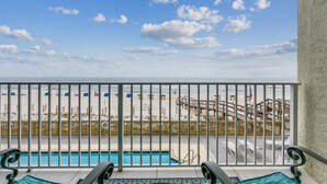 A balcony with a view of a beach, a pool, and a wooden deck with lounge chairs. - BEST DEAL ON THE KEY! Updated Gulf Front Condo! Full Ocean Views! (Pensacola)