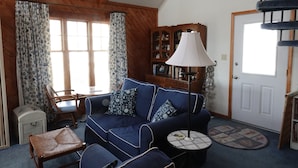 Ein gemütliches Wohnzimmer mit einem blauen Sofa, einem kleinen Tisch, einer Lampe und einem Bücherregal.