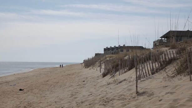 Ein sandiger Strand mit einer Holzlattenzaun und Gebäuden im Hintergrund.