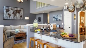 A modern kitchen with a central island, bar stools, a dining area with a sofa, and a world map on the wall. - Pikes Peak Views! Fire Pit, Pool Table & Arcade ~ 4 King Beds, Dogs OK! (Colorado Springs)