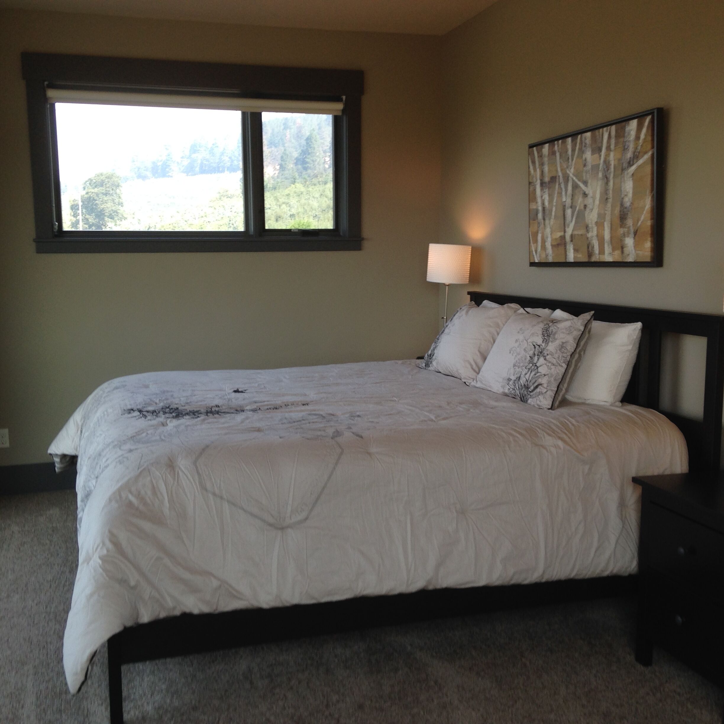 A bedroom with a large bed, a window, a bedside lamp, and a wall-mounted painting.