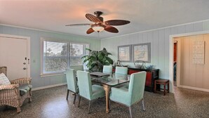 A dining area with a glass table, four chairs, a ceiling fan, and a large window.
