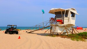 A lifeguard tower with a wheelchair ramp, a beach lifeguard vehicle, and beach umbrellas.