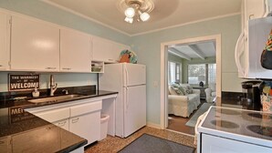 A compact kitchen with white cabinets, a refrigerator, and a sink. There's a sign on the wall that reads "THE WARMEST OF WELCOME".