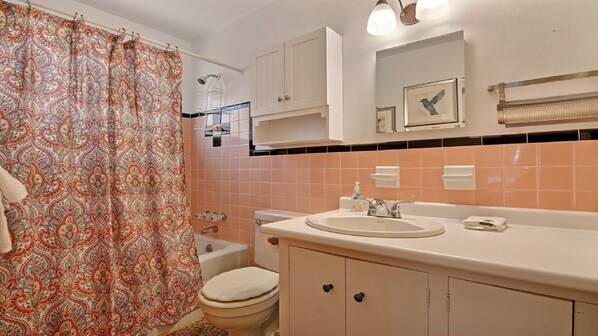A bathroom with a patterned shower curtain, a toilet, a sink with a mirror above it, and cabinets.