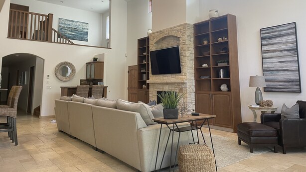 A spacious living room with a high ceiling, a stone fireplace, and a large TV mounted on the wall. - Spacious home in Carmel: one mile to downtown.  (Carmel-By-The-Sea)