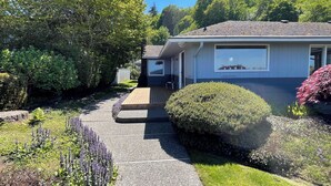 Une maison dotée d’un porche abrité, d’une petite terrasse et d’un jardin où poussent diverses plantes et fleurs.