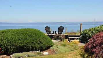 Une vue d’un jardin avec deux chaises Adirondack donnant sur un plan d’eau, une terrasse en bois et une montagne à l’horizon.
