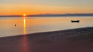 Un coucher de soleil sur une étendue d’eau calme, avec un bateau et des montagnes au loin.
