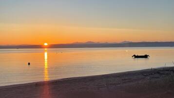 Un coucher de soleil sur une étendue d’eau calme, avec un bateau et des montagnes au loin.