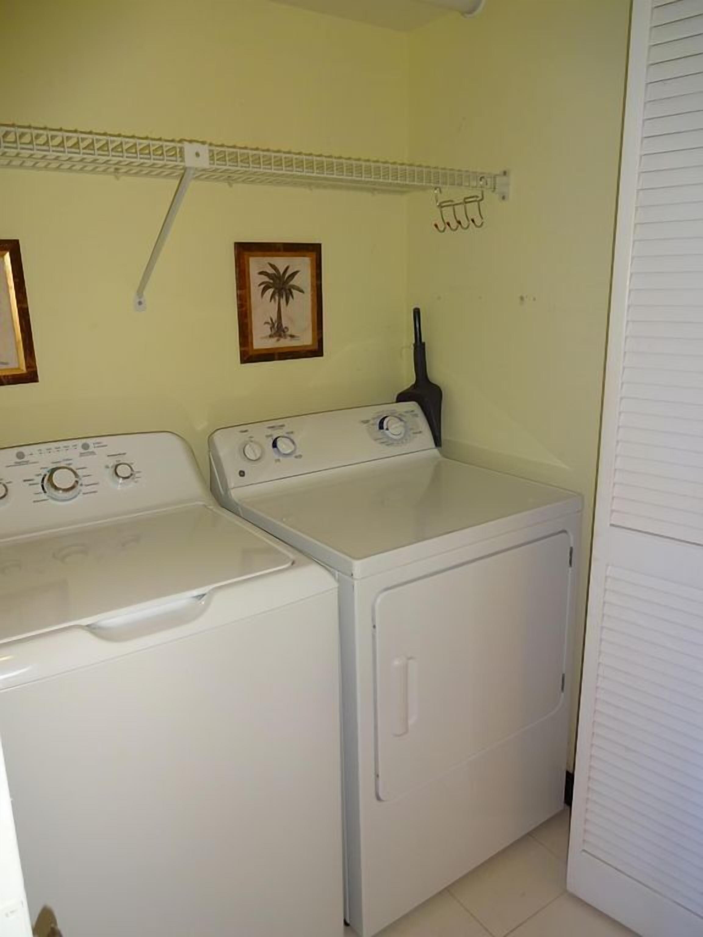A laundry room with two white washing machines, a shelf above, and a framed picture on the wall.