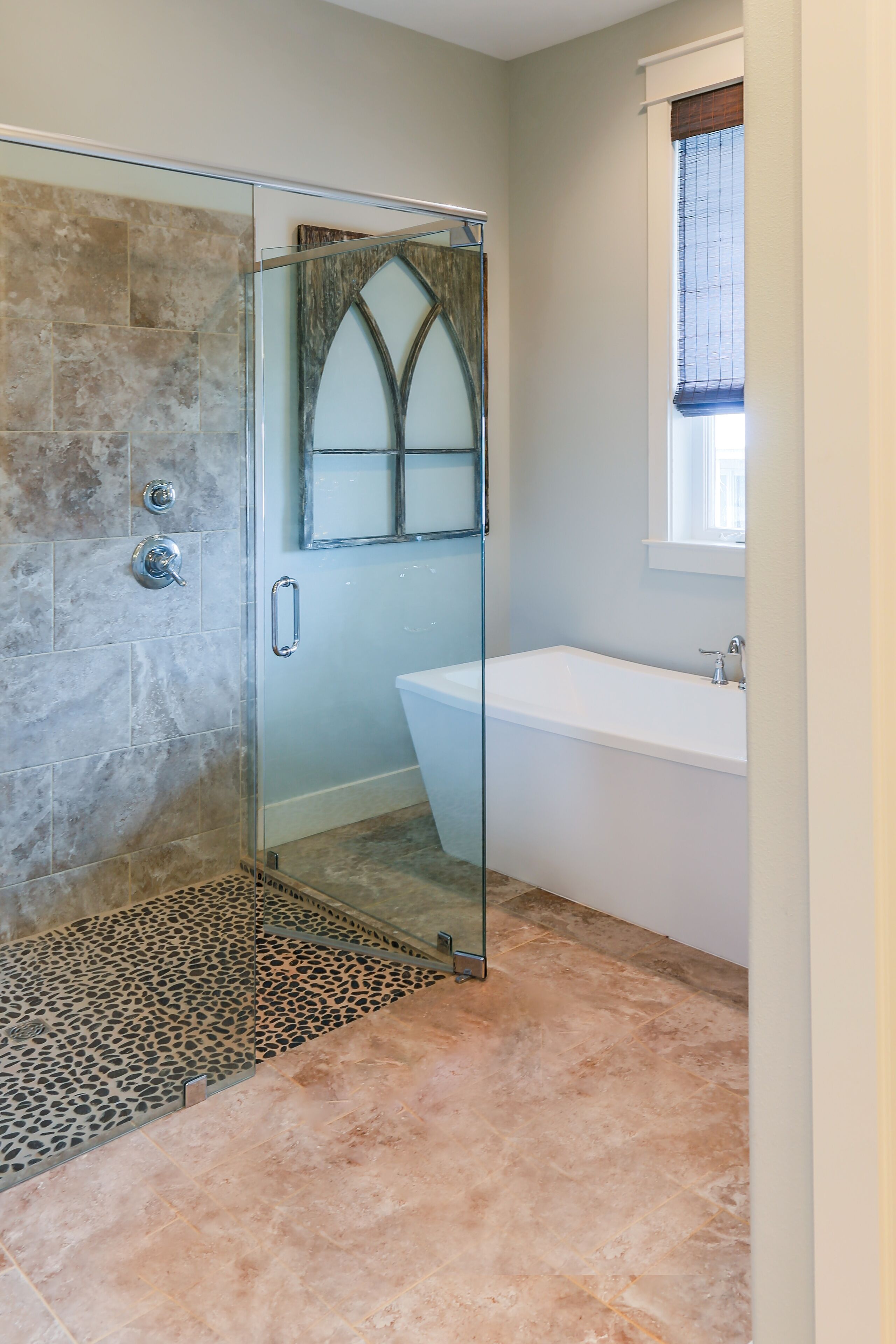 Une salle de bain avec une douche à parois de verre, une baignoire et une fenêtre équipée de stores.