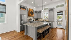Une cuisine spacieuse dotée d’un grand îlot central, de meubles gris, d’appareils électroménagers en acier inoxydable et d’un mur d’accent en bois.