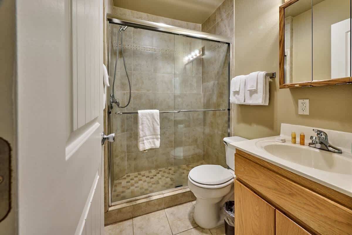 Een badkamer met een douche in een glazen cabine, een toilet, een wastafel met spiegel en een houten kastje.