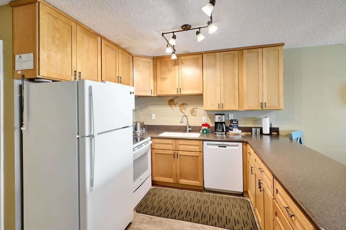 A kitchen with wooden cabinets, a white refrigerator, a dishwasher, and a countertop with various appliances.