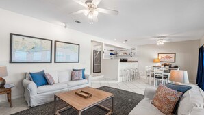 A modern living room with a white sofa, a coffee table, and a kitchen area in the background. - From sunrise surf to sunset sips at Beach Life /Gulf Front, Driect Access to Beach from Balcony (Santa Rosa Beach)