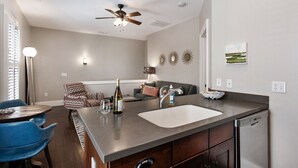 Una cocina moderna con lavavajillas incorporado, un lavamanos grande y un comedor con una silla azul y un sillón estampado.