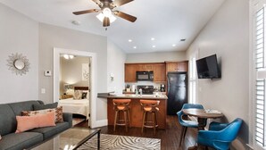 Un espacio habitable compacto con kitchenette, una zona de comedor con taburetes de bar, un sofá y un ventilador de techo.