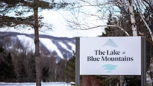 A sign for "The Lake at Blue Mountains" with a mountain and lake view in the background.