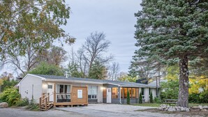 A single-story lodge with a front porch, a covered outdoor seating area, and a gravel driveway.