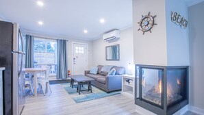 A modern living room with a fireplace, a sofa, a dining table, and a kitchen area.
