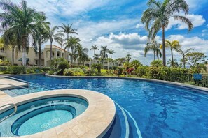 Ein Swimmingpool mit Whirlpool, umgeben von Palmen und einem Gebäude mit weißer Fassade.