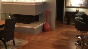 A modern living room with a fireplace, a dining table, and a red vase.