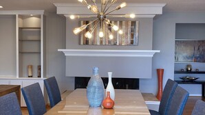 A dining area with a long rectangular table, blue upholstered chairs, and a modern chandelier with multiple light bulbs.