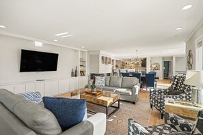Un salon moderne avec un téléviseur à écran plat, des canapés, une table basse et un coin repas à l’arrière-plan.